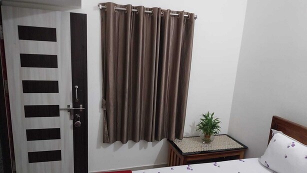 A bedroom with a bed, a bedside table with a plant, a door with a curtain, and a wall with a decorative panel.
