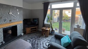Una sala de estar con chimenea, televisor, sofá y vistas al exterior.