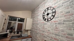 Una cocina con pared de ladrillo, un reloj y un lavavajillas.