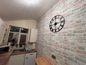 Eine Küche mit Backsteinwand, einer Uhr und einem Geschirrspüler.