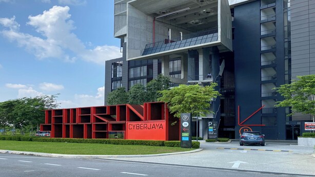 A modern high-rise building with a prominent red structure labeled 'CYBERJAYA' at the base, a parking sign, and a clear sky. - Cyberjaya Tamarind Suites, Mediya Homestay (Cyberjaya)