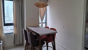 A dining area with a table, chairs, a hanging light fixture, and a view of a cityscape through a window. - Cyberjaya Tamarind Suites, Mediya Homestay (Cyberjaya)