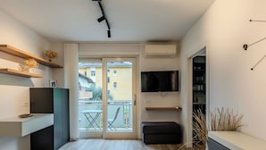 A modern kitchen with a built-in oven, a dining area with a table and chairs, a TV mounted on the wall, and a balcony with a view of the neighborhood. - Family and Friends by Interhome (Riva del Garda)