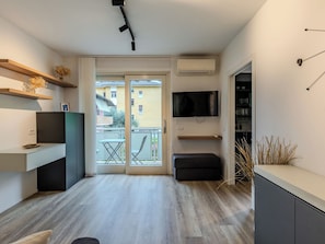 A modern kitchen with a built-in oven, a dining area with a table and chairs, a TV mounted on the wall, and a balcony with a view of the neighborhood. - Family and Friends by Interhome (Riva del Garda)