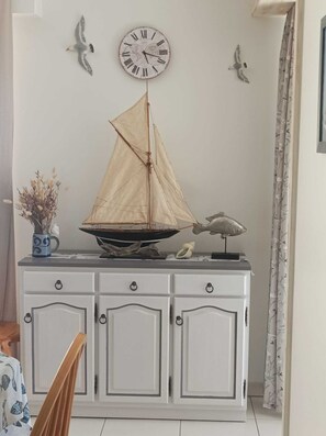 A room with a white cabinet, a decorative sailboat model, a wall clock, and two wall-mounted bird sculptures. - APARTMENT FROND DE MER (La Turballe)