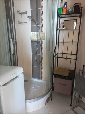 A bathroom with a shower, toilet, and shelves with toiletries. - APARTMENT FROND DE MER (La Turballe)