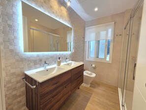 Une salle de bain avec un meuble-lavabo à deux vasques, des toilettes, un espace douche et une fenêtre avec vue.
