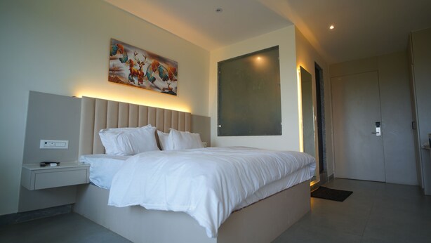 A modern bedroom with a large bed, bedside tables, a wall-mounted painting, and a door.