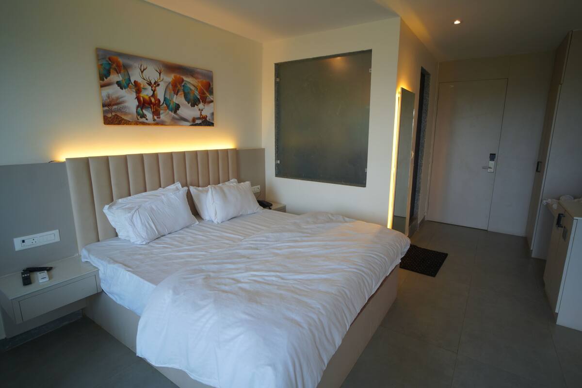 Une chambre d’hôtel moderne avec un grand lit, une table de chevet, une œuvre d’art accrochée au mur et une porte.