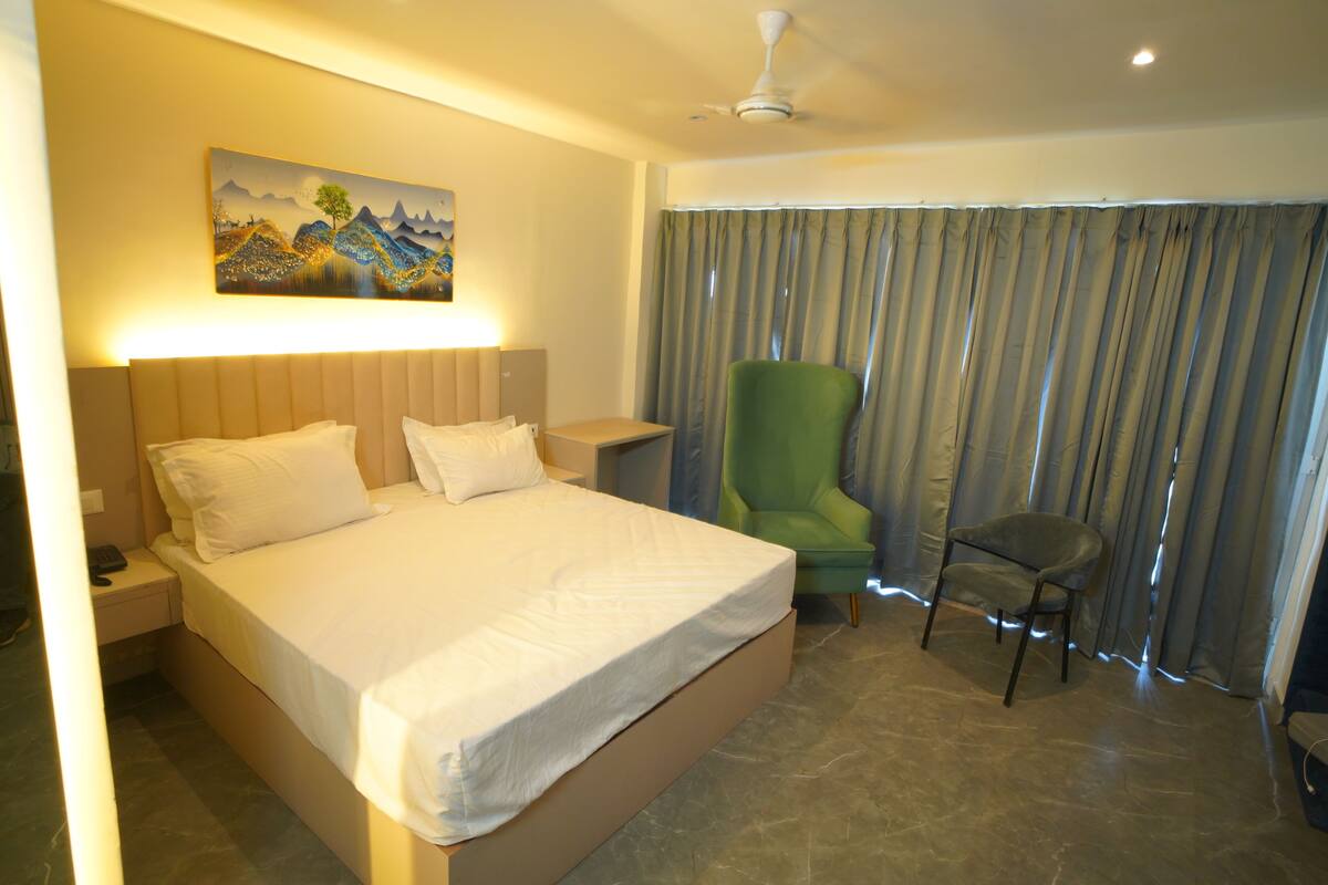 Une chambre d’hôtel avec un grand lit, un fauteuil vert, une petite table et un tableau accroché au mur.