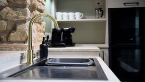 Une cuisine avec un mur en pierre, un évier avec un robinet doré, une machine à café et un four noir.