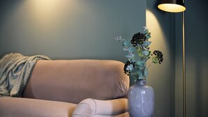 Un canapé beige, une petite table ronde avec un vase de fleurs et une lampe sur pied.