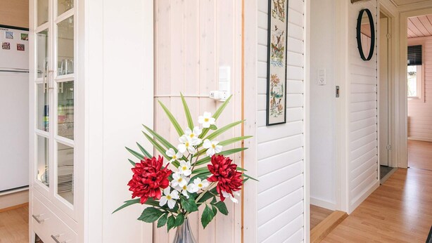 Een hal met een houten vloer, een witte deur en een vaas met bloemen.