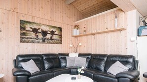 Een zwarte leren modulaire bank met een witte salontafel ervoor, houten vloeren en een houten wand met een schilderij.