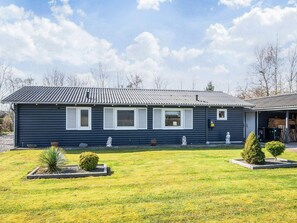 A single-story building with a dark exterior, a sloped roof, and a front yard with a lawn and two small bushes. - 5 Person Holiday Home in Hemmet (Hemmet)