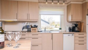 Een moderne keuken met lichte houten kastjes, een vaatwasser en een raam met uitzicht.