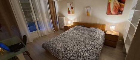 Hotelkamer met een bed, bureau, stoel, raam met gordijnen, een radiator en wanddecoratie.