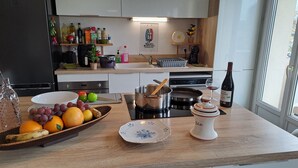 Et køkken med en frugtfat, en vinflaske og forskellige køkkenartikler på bordet.