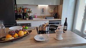 Une cuisine avec un plateau de fruits, une bouteille de vin et divers ustensiles de cuisine sur le comptoir.