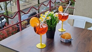 En balkon med et træbord, to stole, en potteplante og to drikkevarer med appelsinskiver.