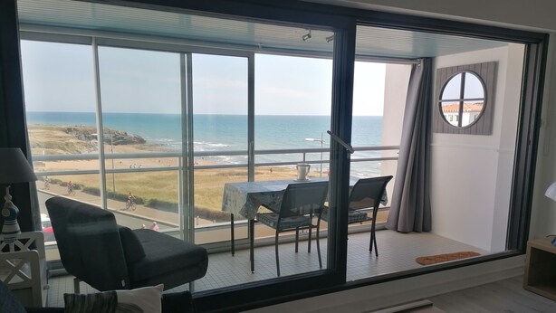 Uma varanda com vista para a praia e o oceano, uma mesa com cadeiras e um sofá.