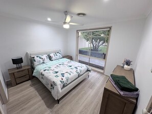 Quarto com cama, mesa de cabeceira, janela e ventilador de teto.
