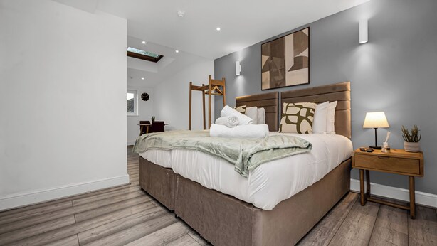 Ein modernes Schlafzimmer mit einem großen Bett, Nachttischen, einer Wanduhr und einer Deckenleuchte.