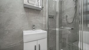 Ein Badezimmer mit einer Duschkabine, einem weißen Waschbecken und einem Spiegel darüber.