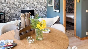 Una stanza con carta da parati a motivi floreali, un tavolo rotondo in legno con un vaso di fiori gialli, un letto con una parete blu e una porta decorata con motivi a foglia.