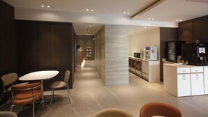 A modern hotel lobby with a reception desk, seating area, and a kitchenette.