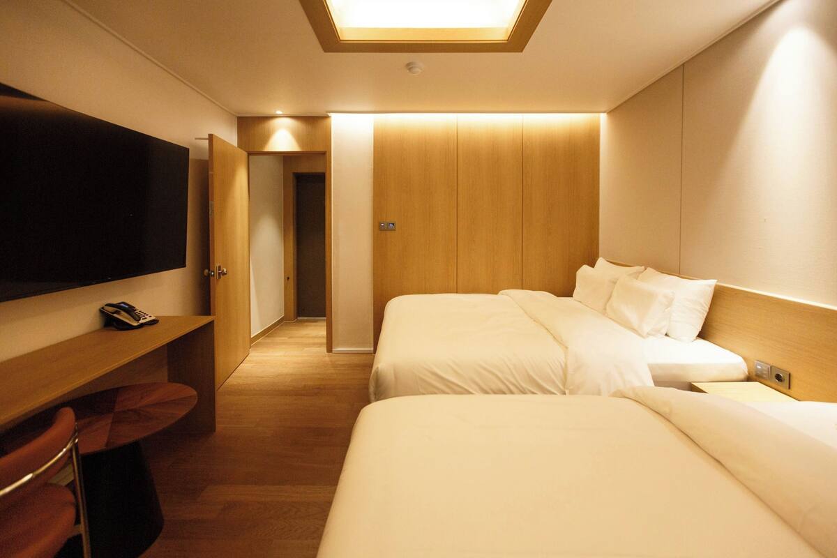 Ein Hotelzimmer mit zwei Betten, einem Fernseher, einem Schreibtisch und einem Holzschrank.