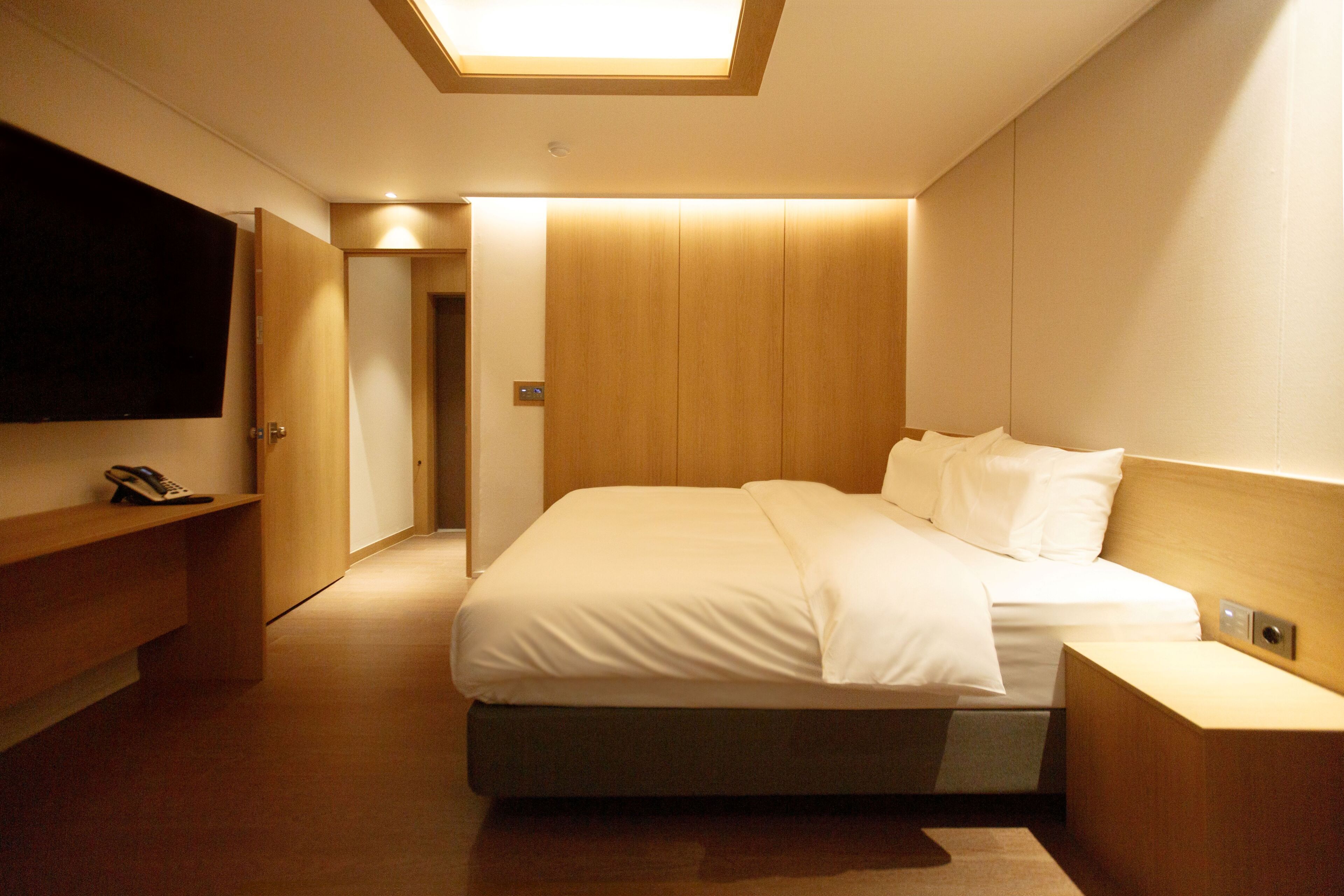 Ein modernes Hotelzimmer mit einem großen Bett, Nachttischen, einem Flachbildfernseher und einem Holzschrank.