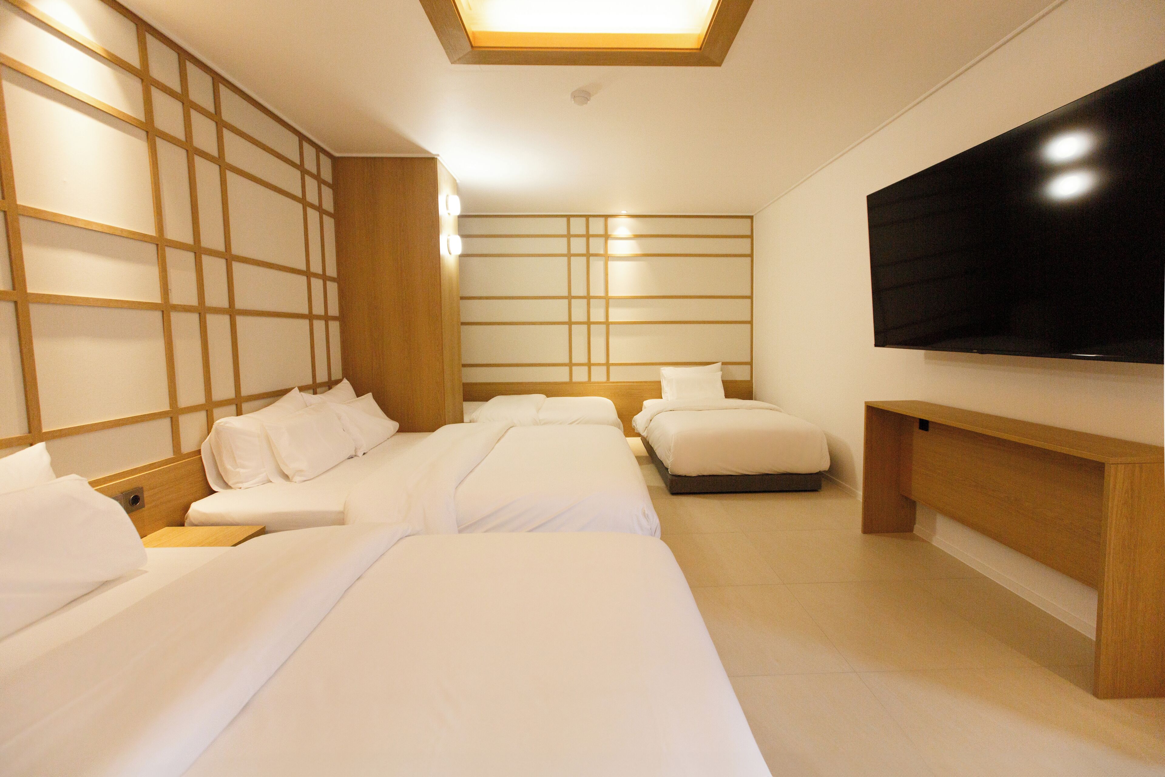 Une chambre d’hôtel avec trois lits, un téléviseur à écran plat et une tête de lit en bois.