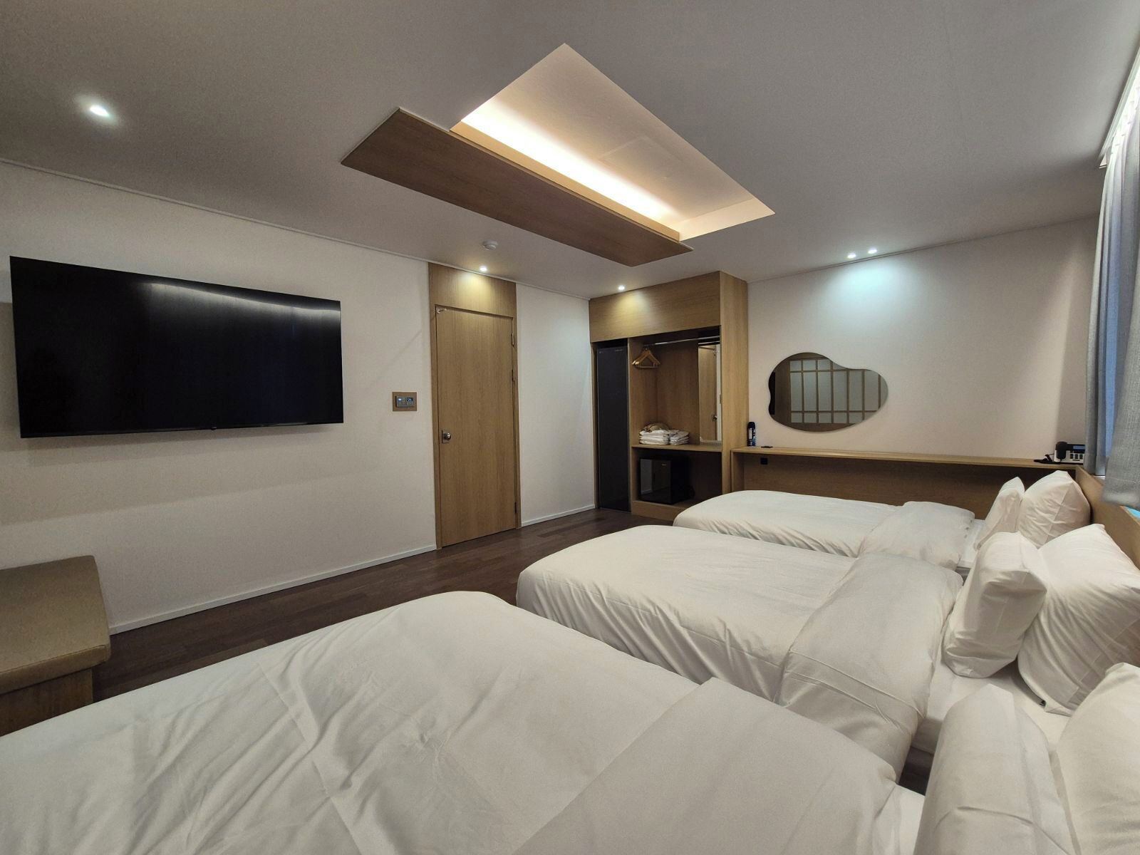Quarto de hotel com televisão de ecrã plano, guarda-roupa, espelho e duas camas.