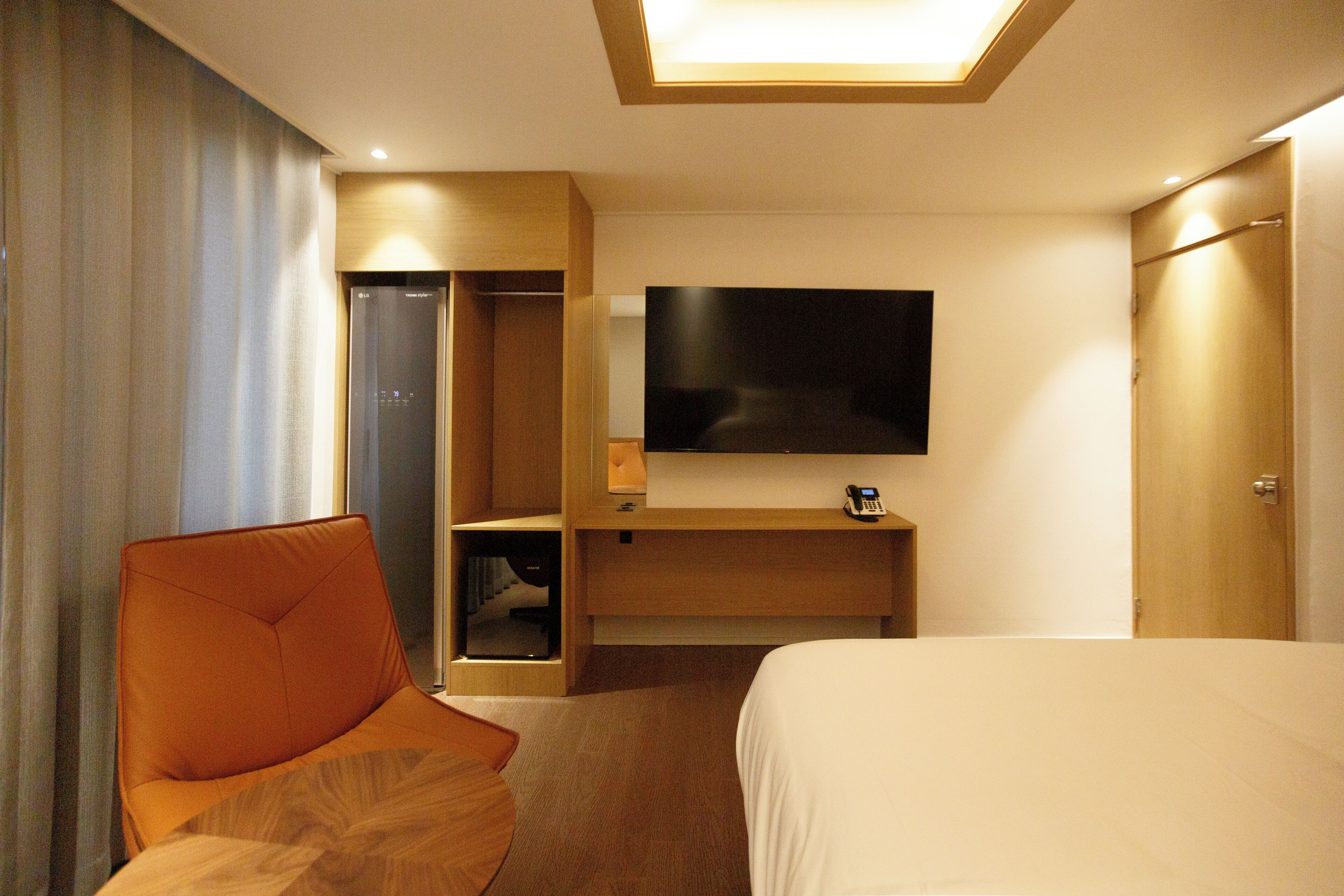 Une chambre d’hôtel comprenant un lit, un téléviseur fixé au mur, une armoire en bois et un coin salon avec un fauteuil.