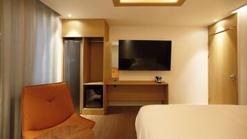 Une chambre d’hôtel comprenant un lit, un téléviseur fixé au mur, une armoire en bois et un coin salon avec un fauteuil.