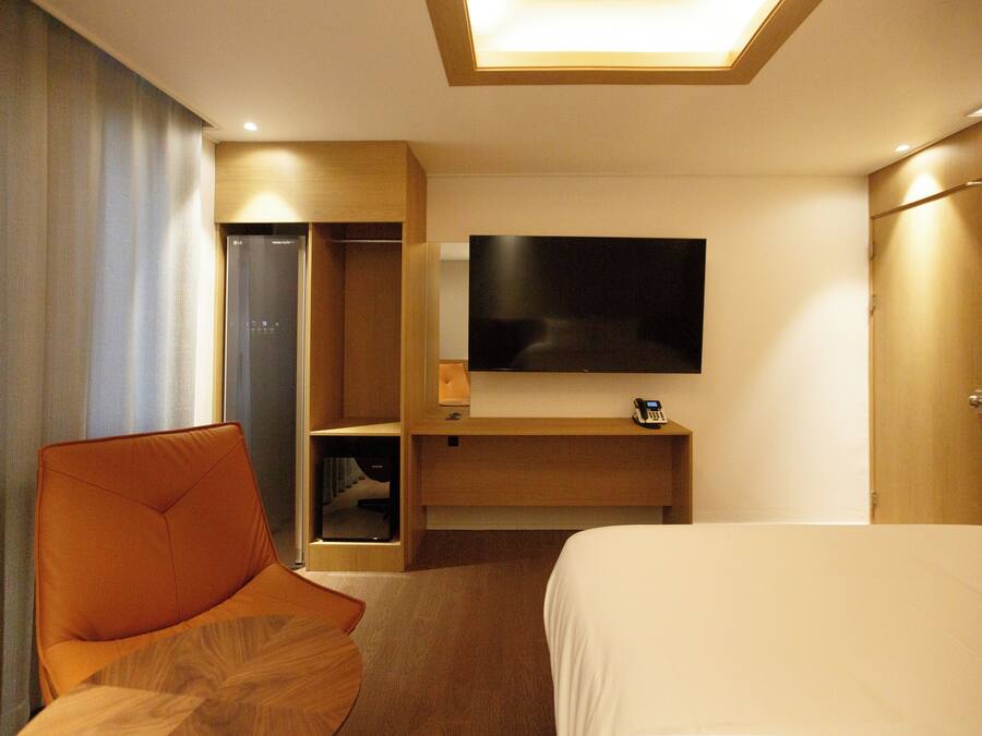 Une chambre d’hôtel comprenant un lit, un téléviseur fixé au mur, une armoire en bois et un coin salon avec un fauteuil.