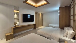 A modern hotel room with a flat-screen TV mounted on the wall, a wooden headboard, two beds with white bedding, and a ceiling light fixture.