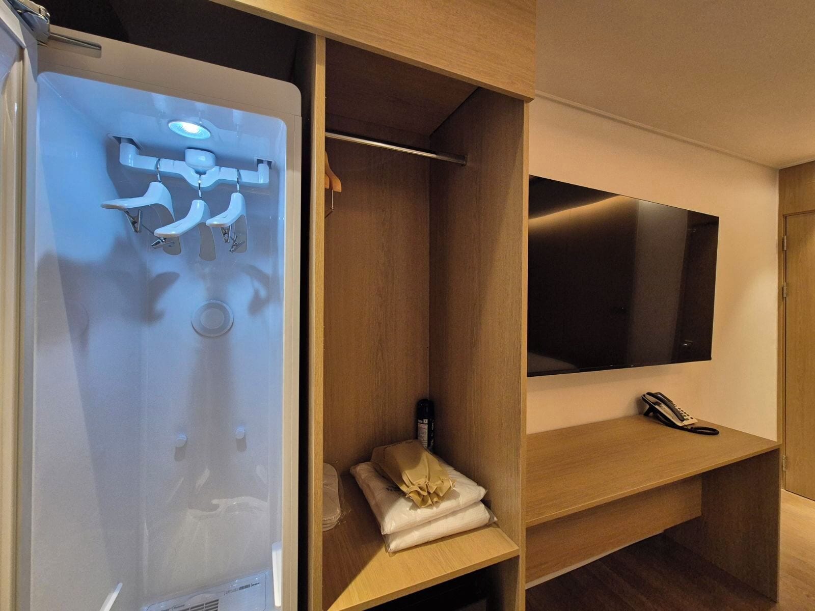 Une salle de bain moderne avec une douche à parois de verre, un meuble-lavabo en bois avec un miroir et un téléviseur à écran plat fixé au mur.