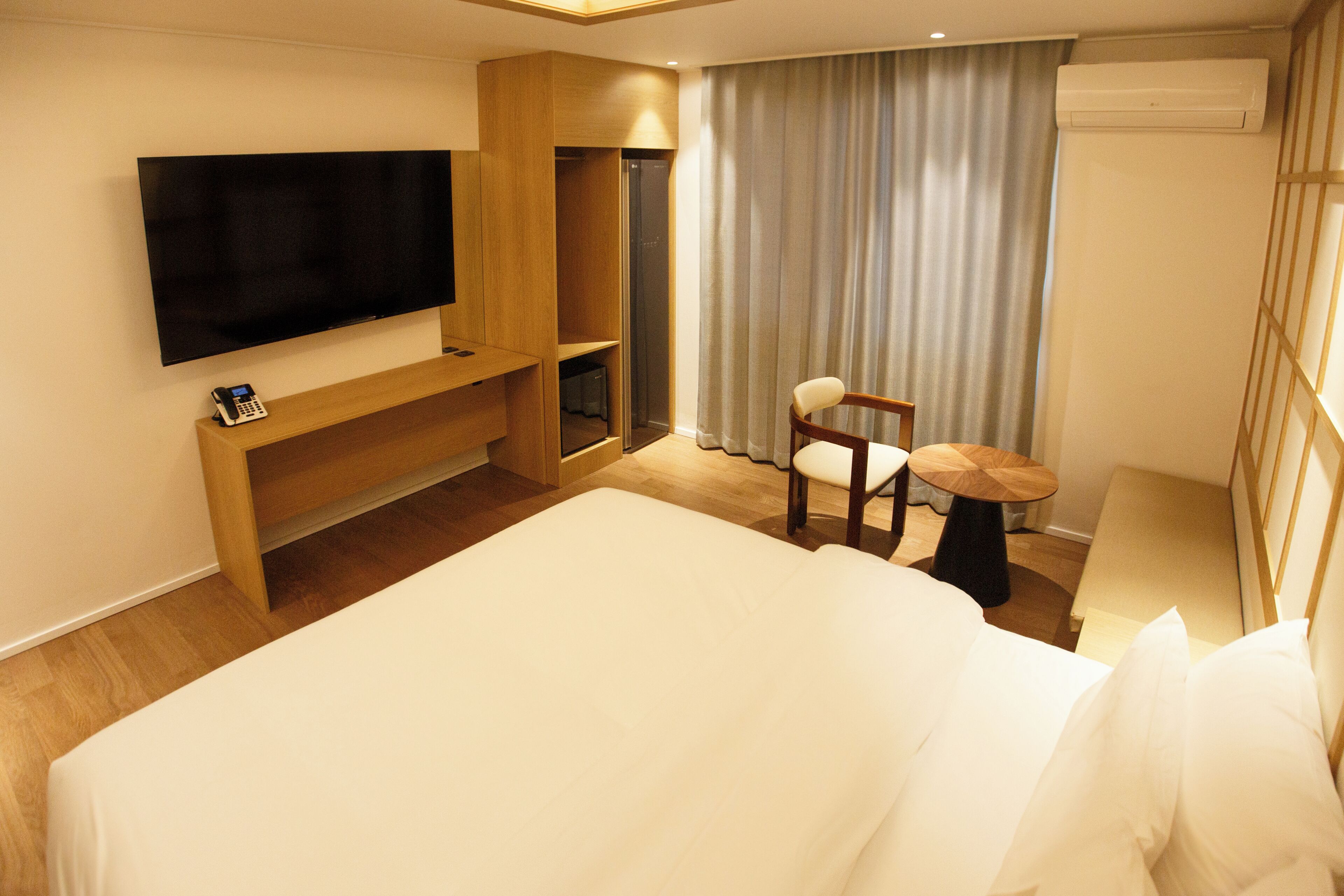 Une chambre d’hôtel avec un grand lit, un téléviseur fixé au mur, un bureau avec une chaise et une fenêtre avec des rideaux.
