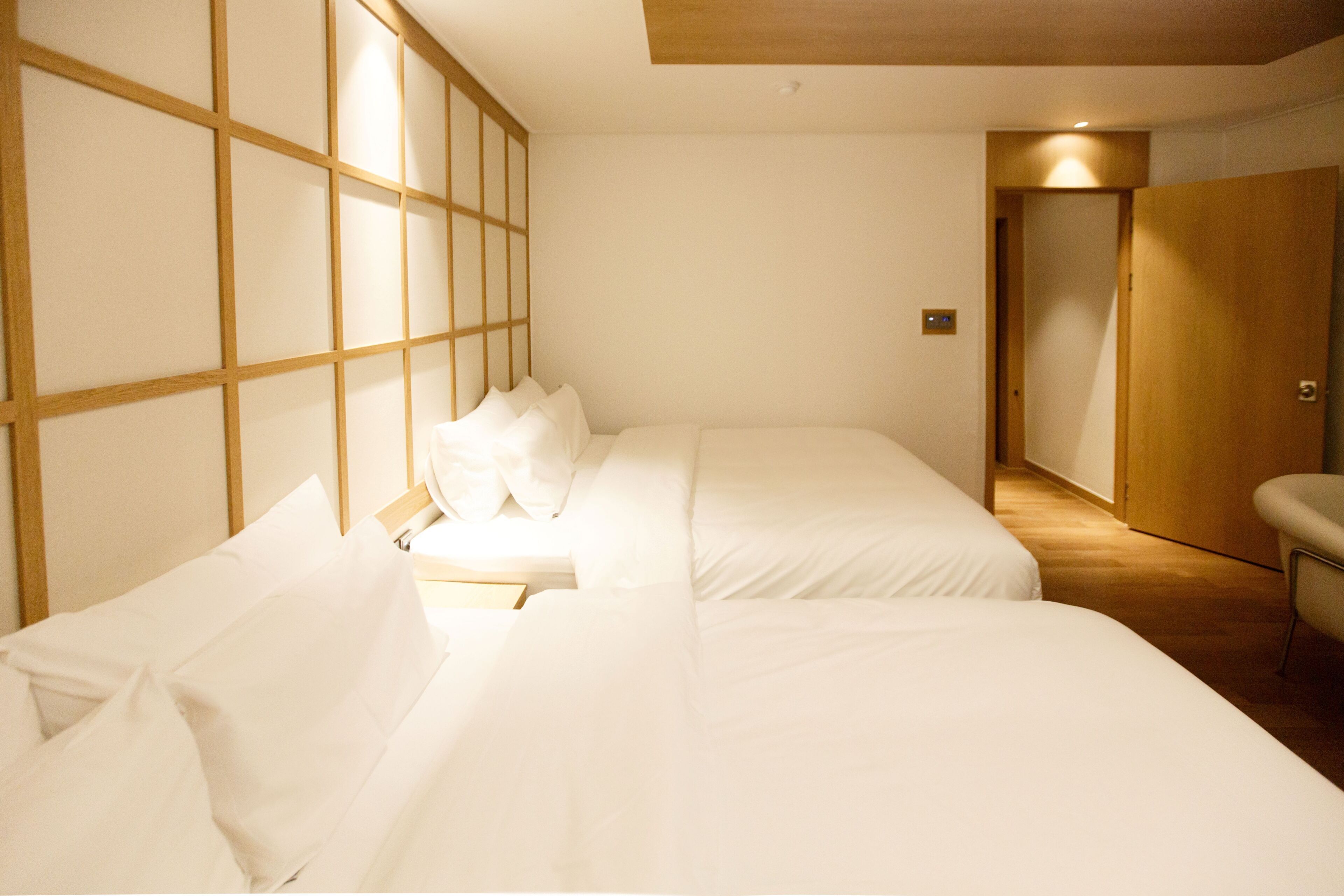 A hotel room with two beds, a wooden partition wall, a wooden door, and a chair.