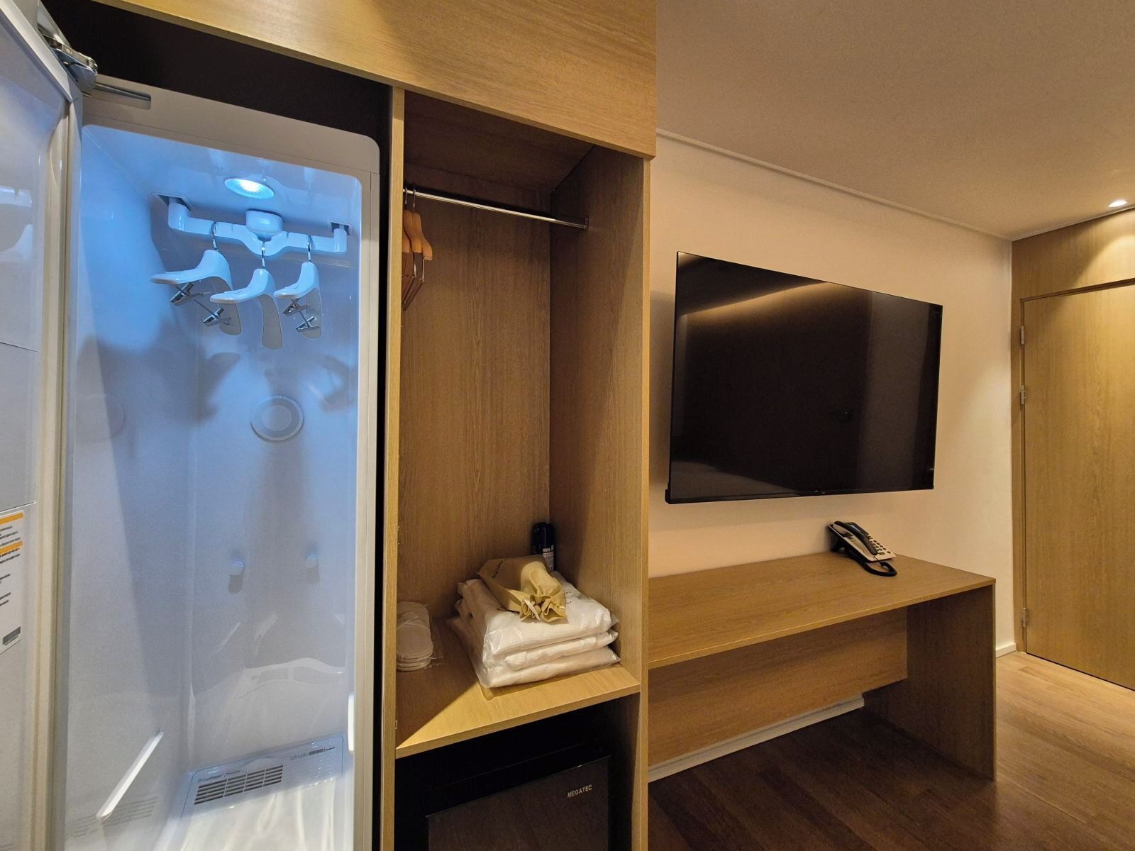 A modern bathroom with a shower, a towel rack, a mounted TV, and a telephone.