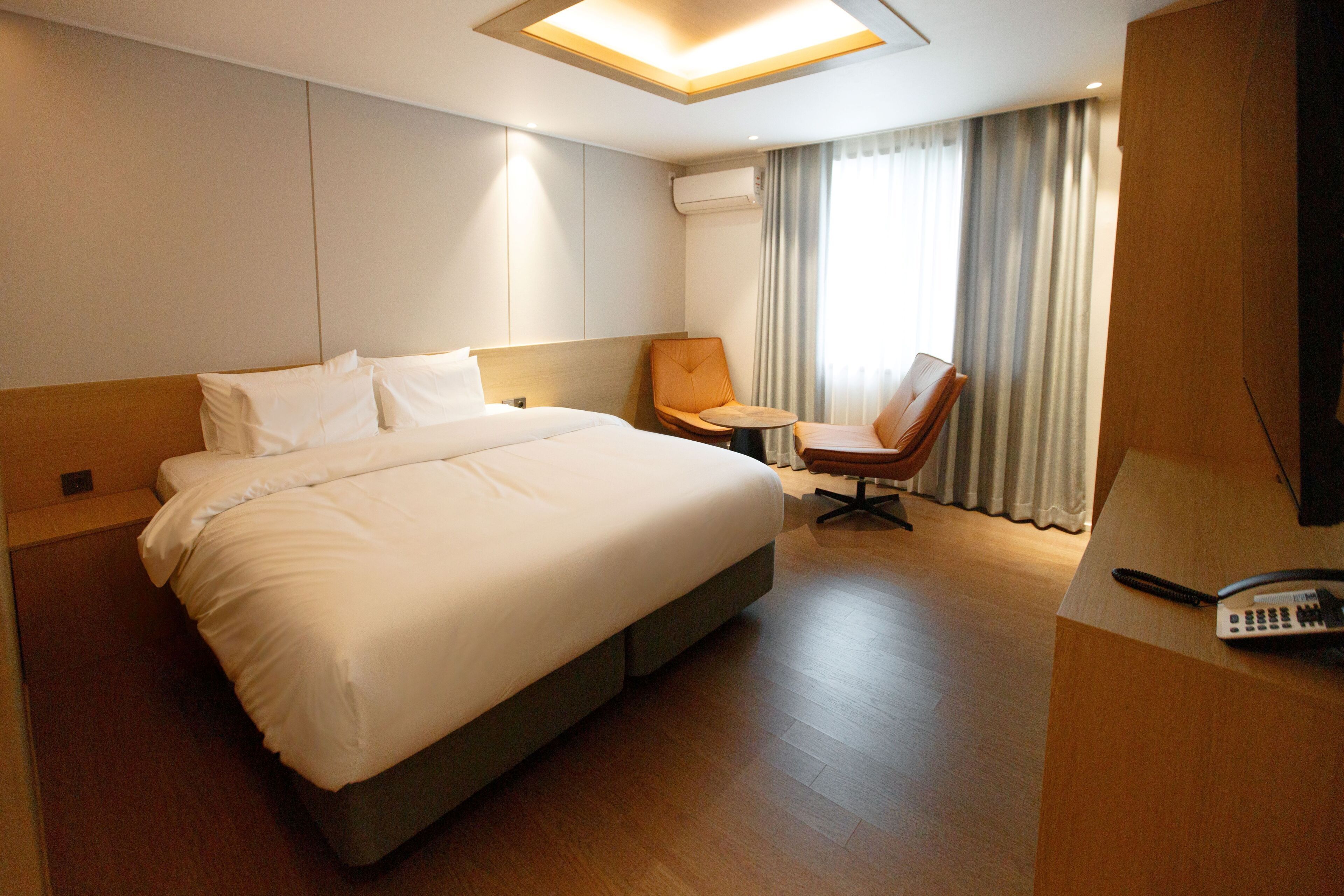 Habitación de hotel con una cama grande, un escritorio con teléfono, una silla y una ventana con cortinas.