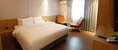 Habitación de hotel con una cama grande, un escritorio con teléfono, una silla y una ventana con cortinas.