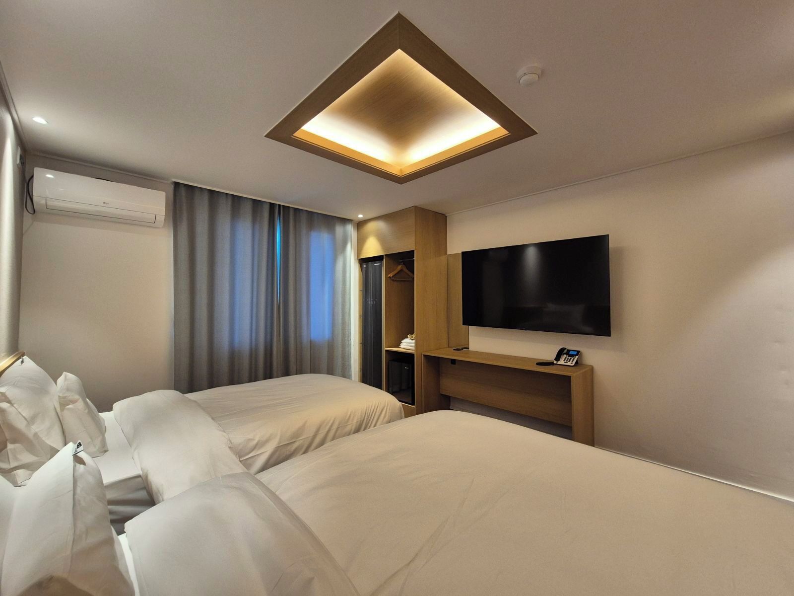 A hotel room with two beds, a flat-screen TV, a wardrobe, and a ceiling light fixture.