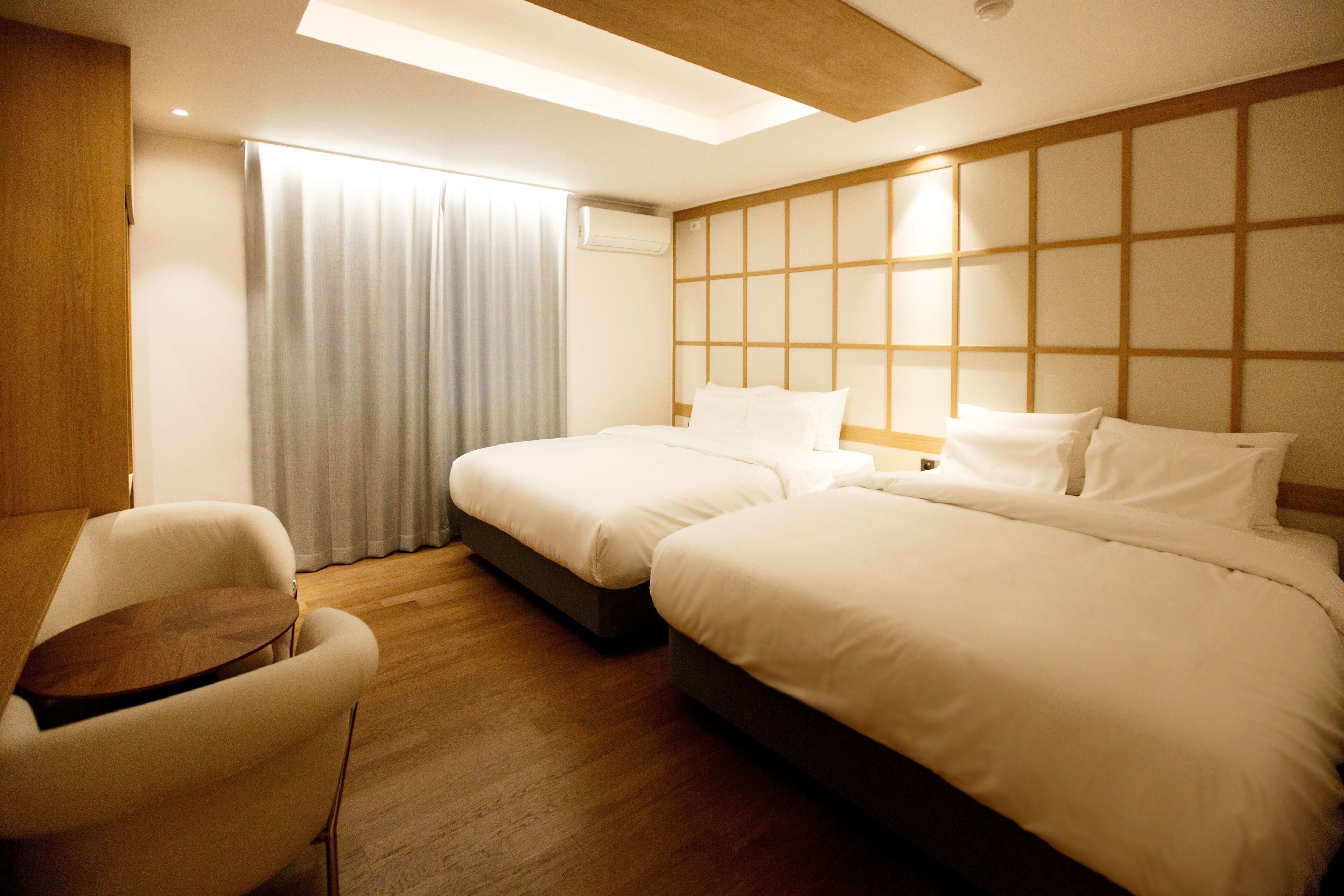 Une chambre d’hôtel avec deux lits, un plancher en bois, un bureau et une fenêtre avec des rideaux.