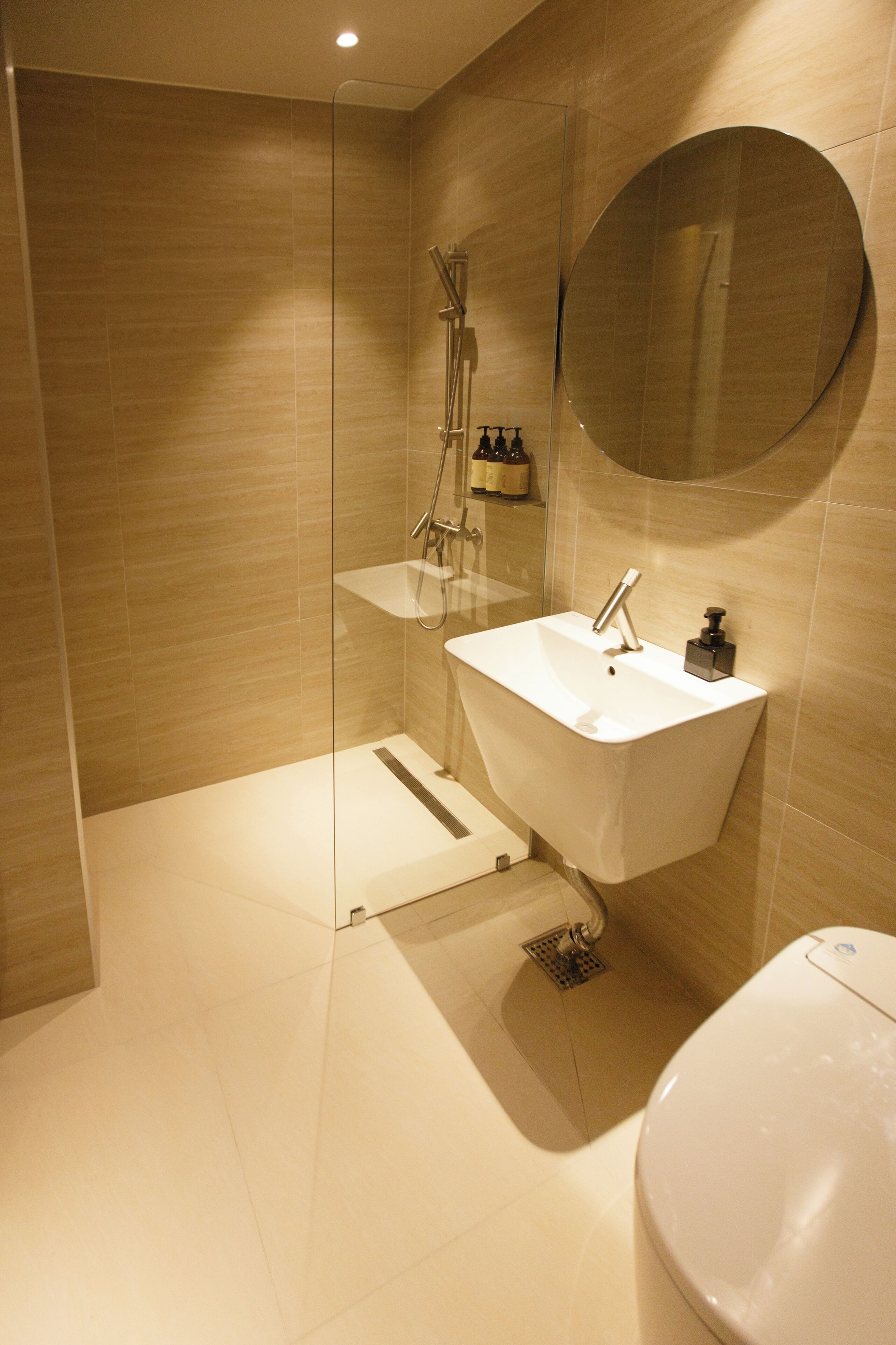 Un baño moderno con ducha de vidrio, lavamanos blanco y espejo redondo.