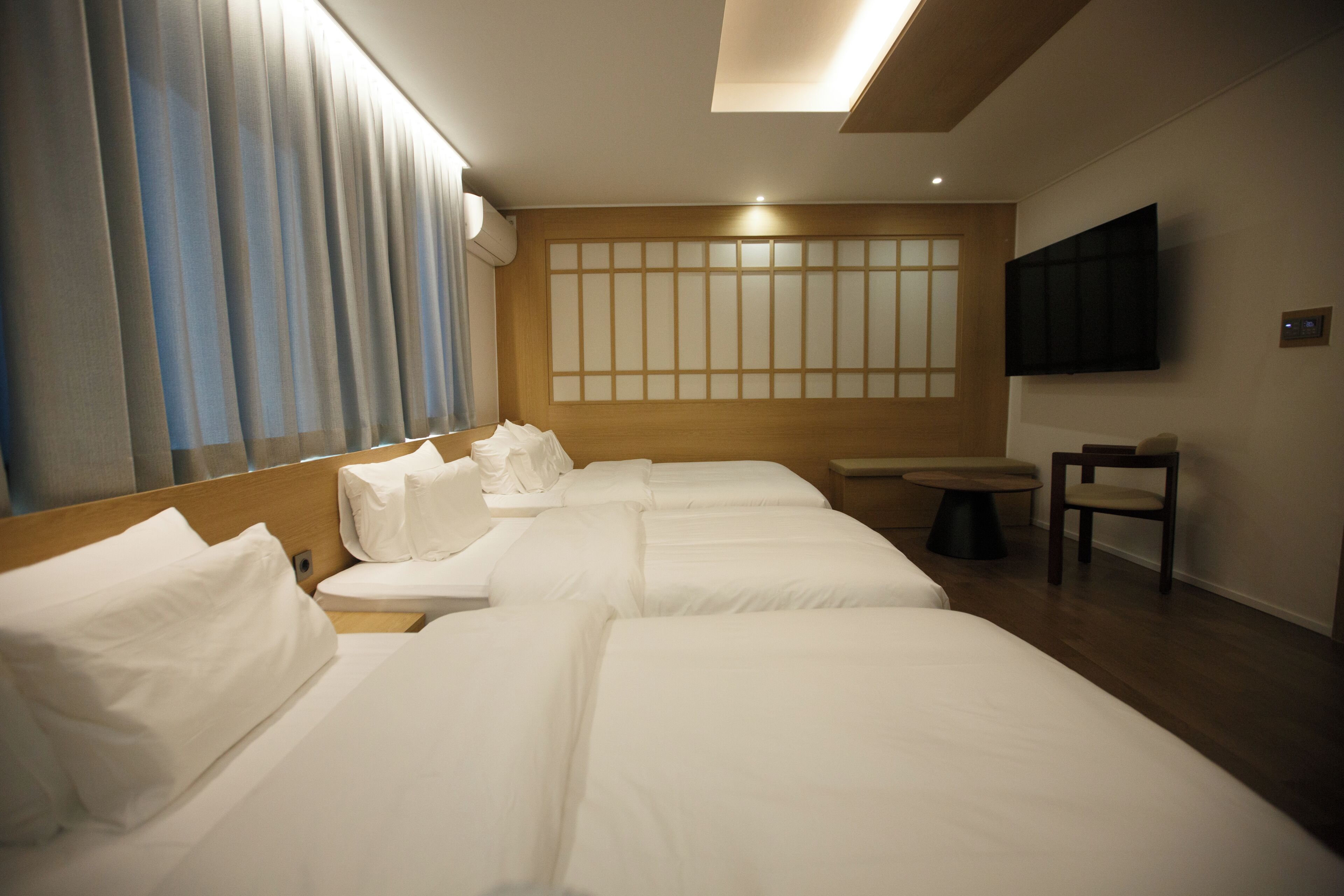 Ein Hotelzimmer mit zwei Betten, einem Wand-Fernseher, einem kleinen Tisch und einem Stuhl.