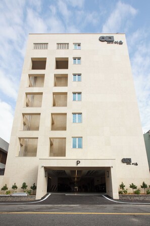A multi-story hotel with a central entrance, a parking area, and a clear sky.
