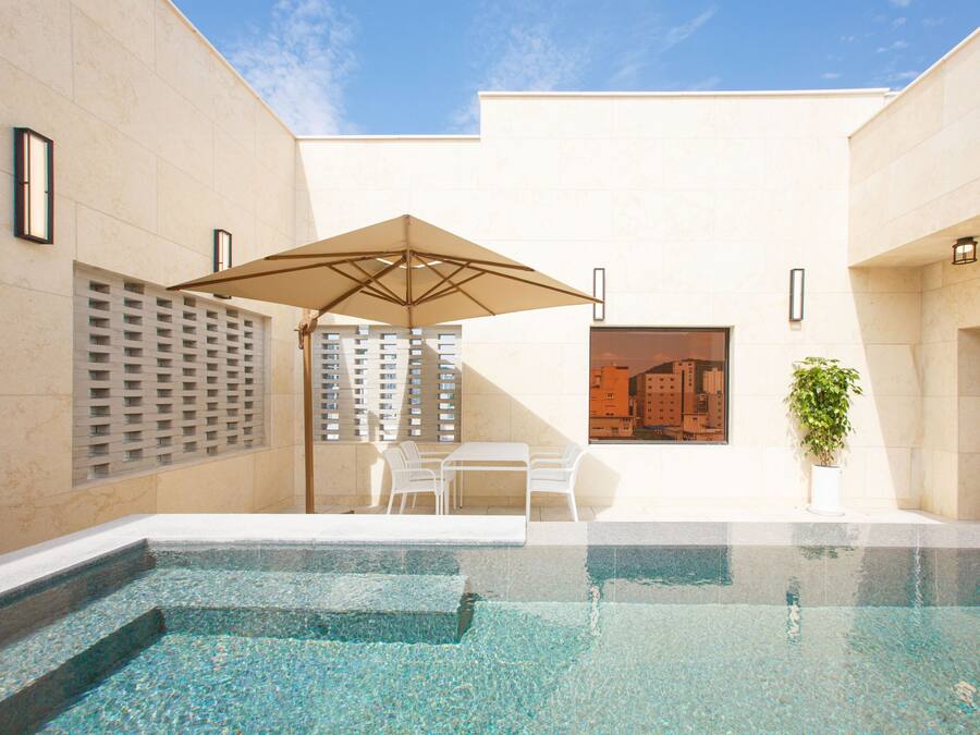 A swimming pool with a table and chairs, a potted plant, and a building in the background.